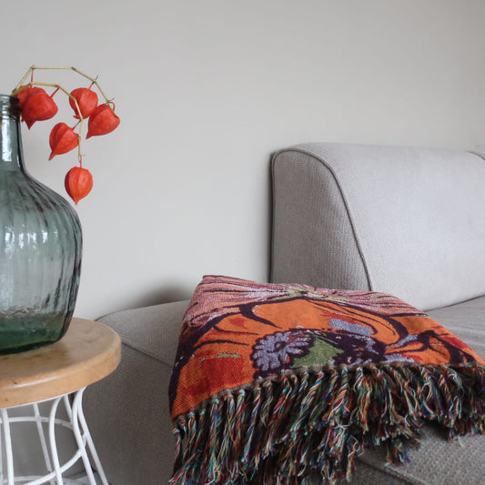 Plaid Peony van Imbarro nonchalant over een bank gedrapeerd, warm en kleurrijk handgemaakt woonaccessoire.